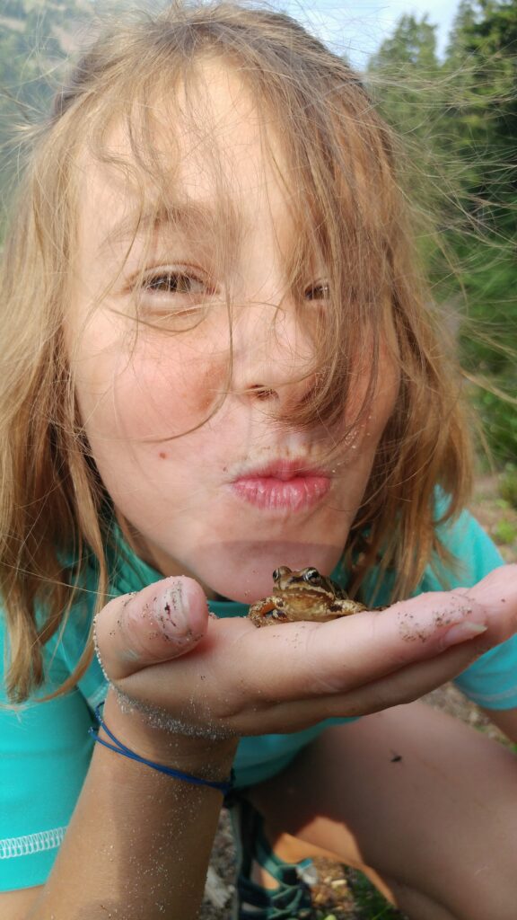 A child holds up a frog in their hand.