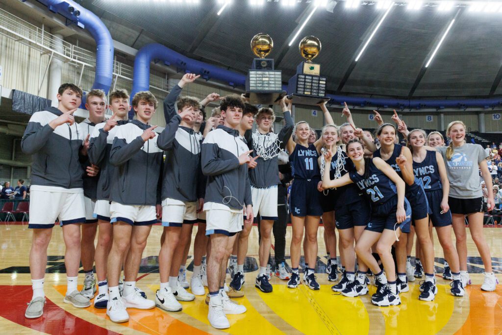 The Lynden Christian boys and girls basketball teams celebrate with both trophies over the crowded huddle.