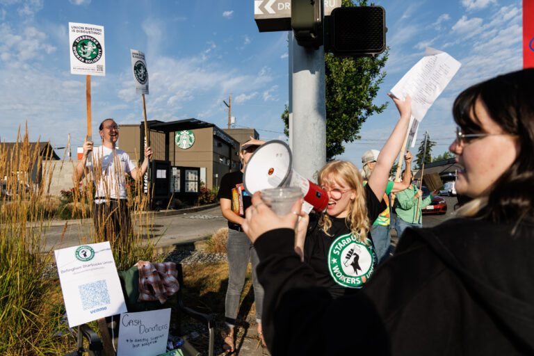 Using a megaphone, Heather Bergeson cheers on unionized Starbucks workers and their supporters as they strike with their protesting signs.