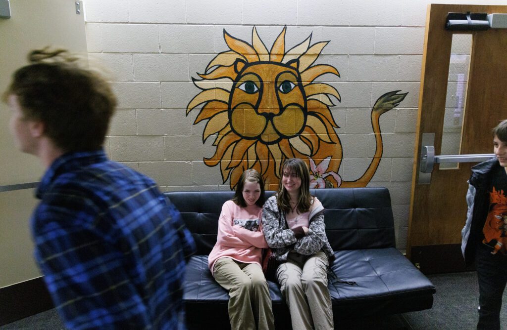 Former Sunnyland Elementary students Run Clark and Lolo Goodenough sit on a bench below a lion mural.