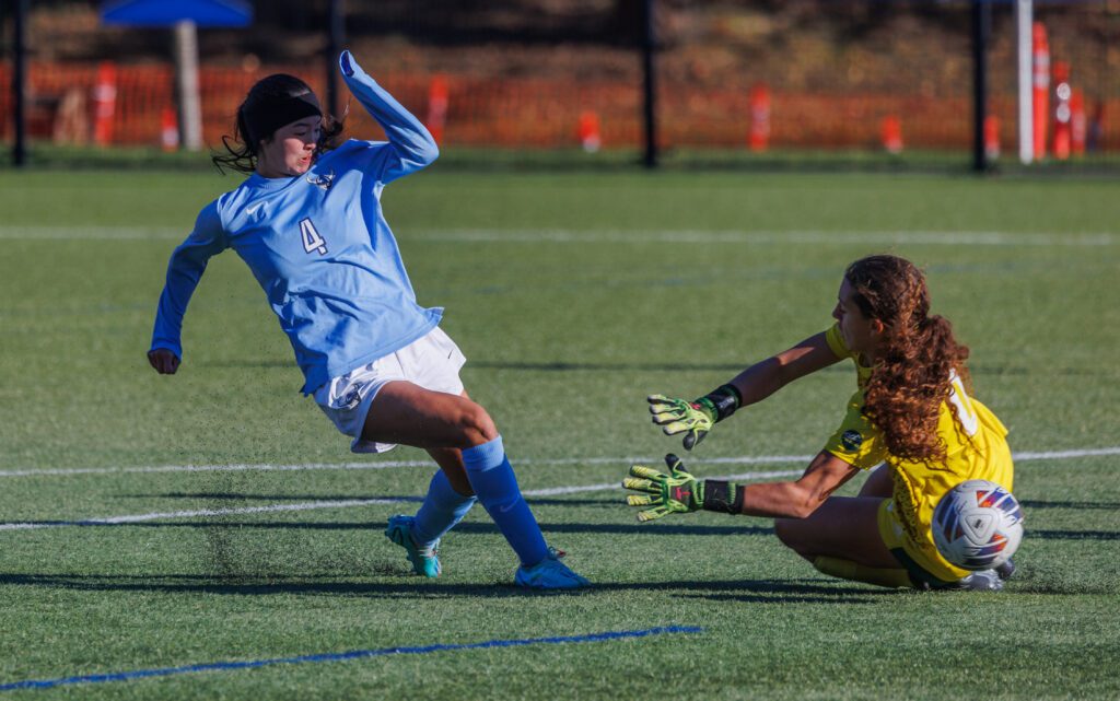 Western Washington University’s Morgan Manalili kicks the ball past Concordia University Irvine’s goalkeeper who is on the ground.