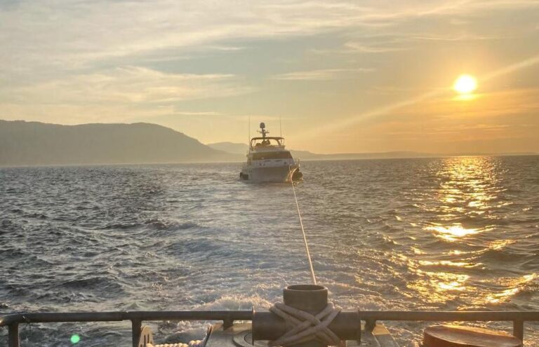 A 45-foot response boat from Coast Guard Station Bellingham tows a vessel as the sun sets over the horizons.