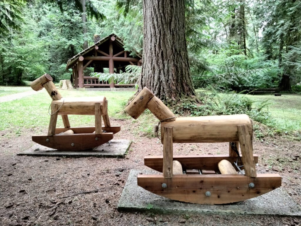 Two wooden rocking horses at a picnic shelter.