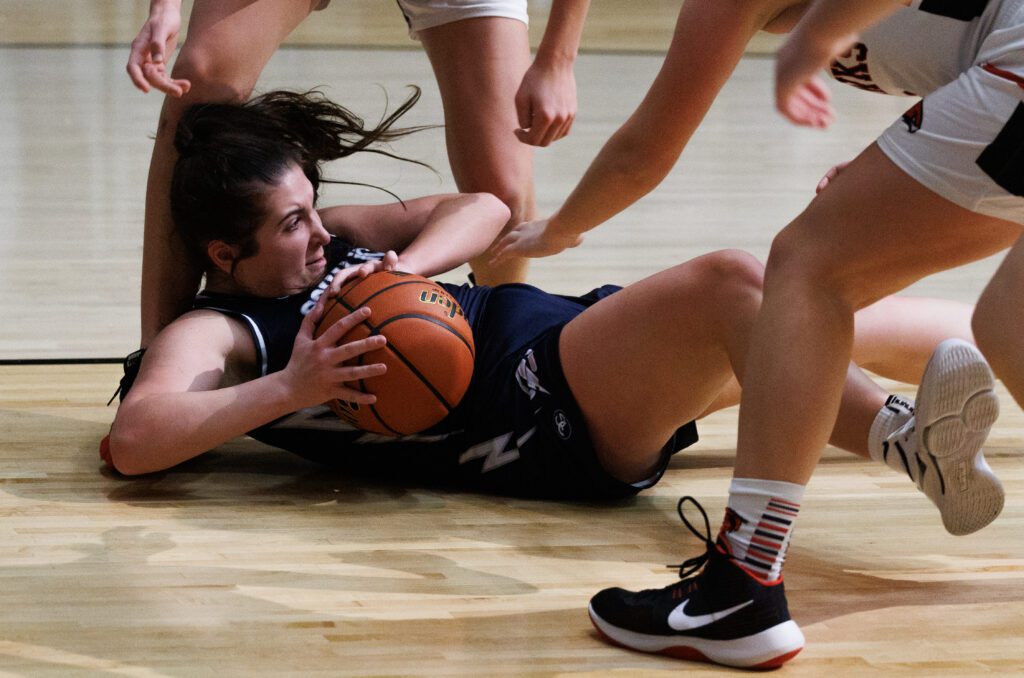 Falling to the floor while grabbing a loose ball, defenders try to reach for the ball.