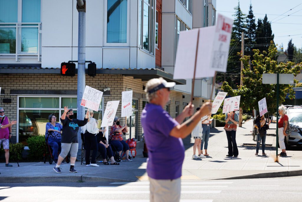 Residents and friends picket outside the Eleanor Apartments with multiple signs.