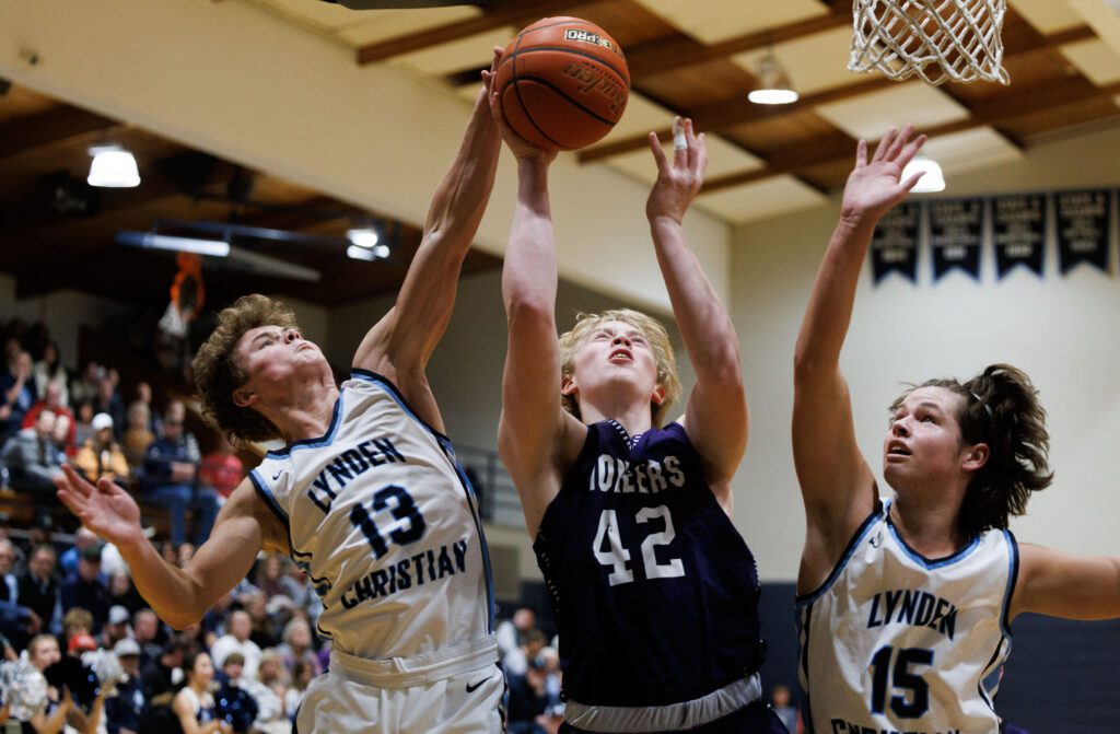 Lynden Christian’s Griffin Dykstra blocks a shot by Nooksack Valley’s Brady Ackerman as another defender looks to take control of the ball.