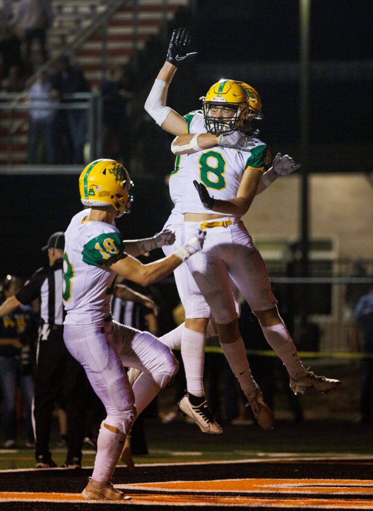 Lynden receiver Isaiah Stanley (8) and a couple of teammates celebrate his touchdown as he is hugged mid-air.