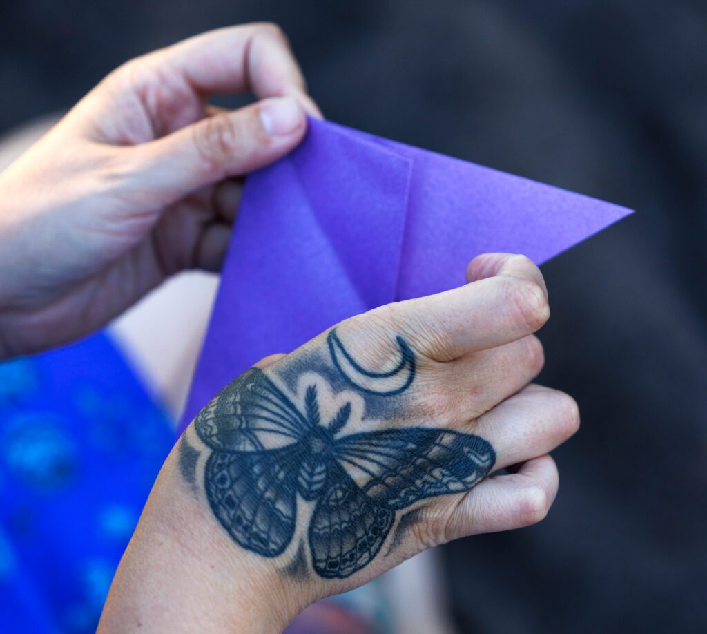 A luna moth is tattooed on the hand of Theresa Warburton as she folds paper into a butterfly.