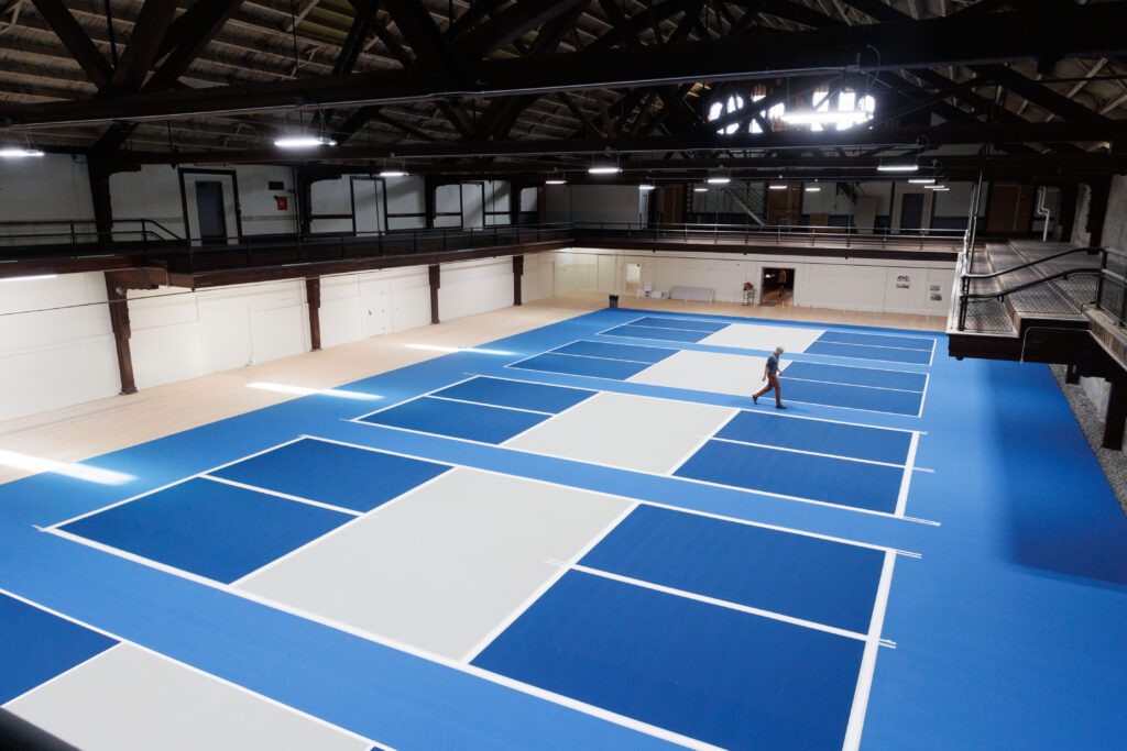 Armory Pickleball co-owner Craig Cooper walks between the bright blue courts.