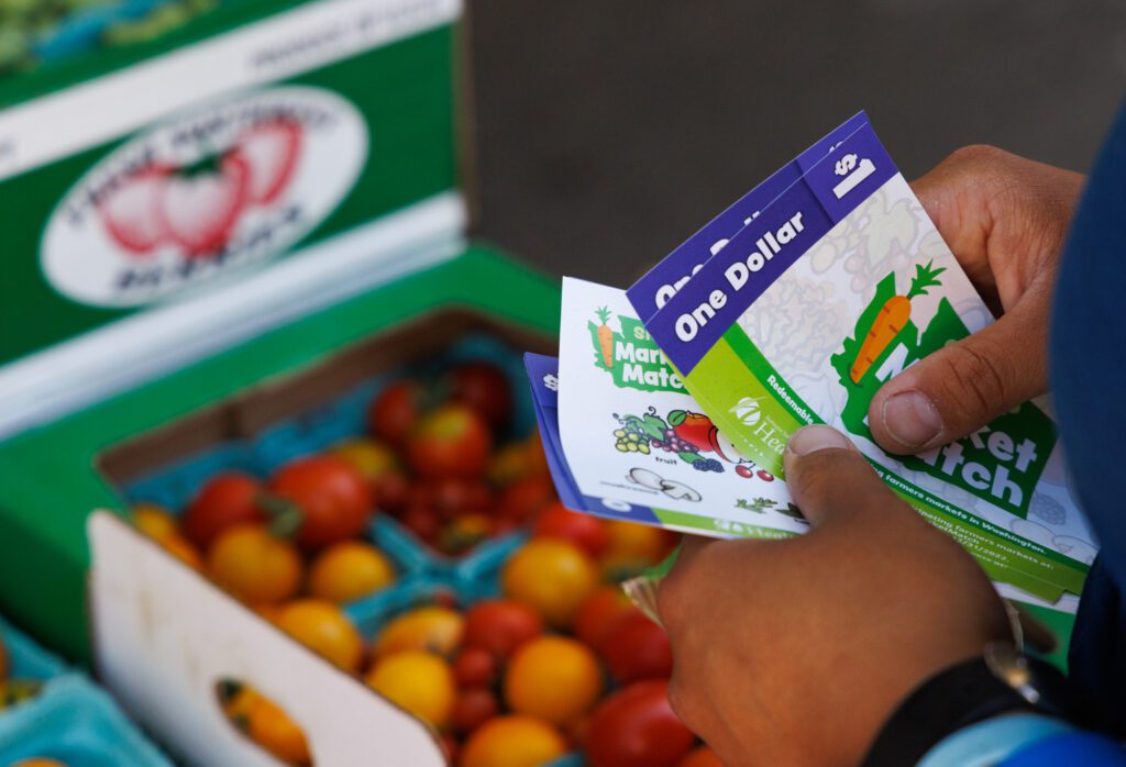 An attendee holds SNAP dollars over crates of fresh produce.