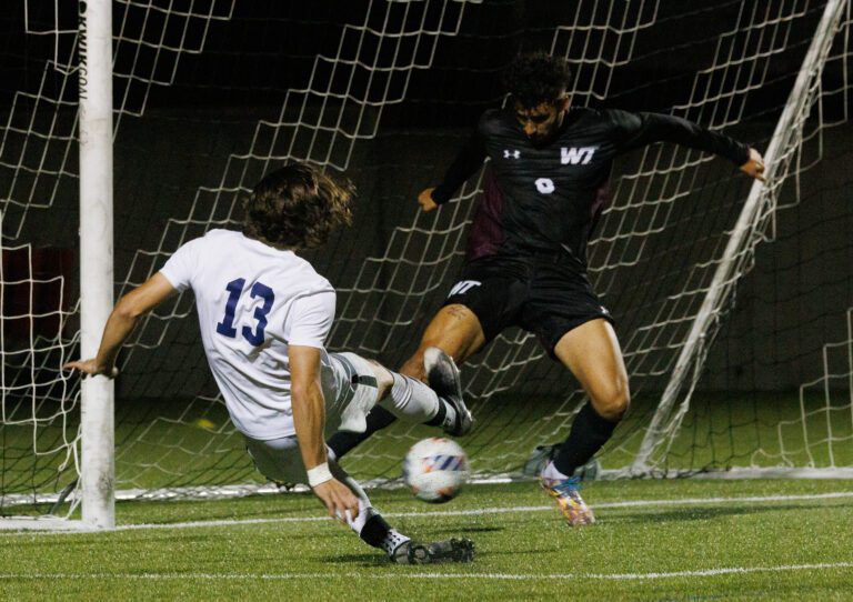 Andrew Rotter takes a shot at the goal as the goalie spreads his limbs to block the shot.