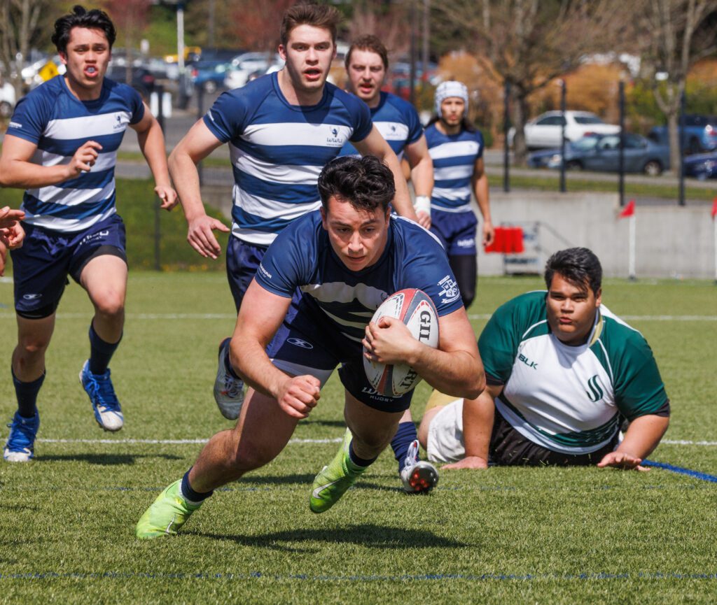 Western Washington University’s Nate Mathis dives as other players are sprinting over while one is on the ground.