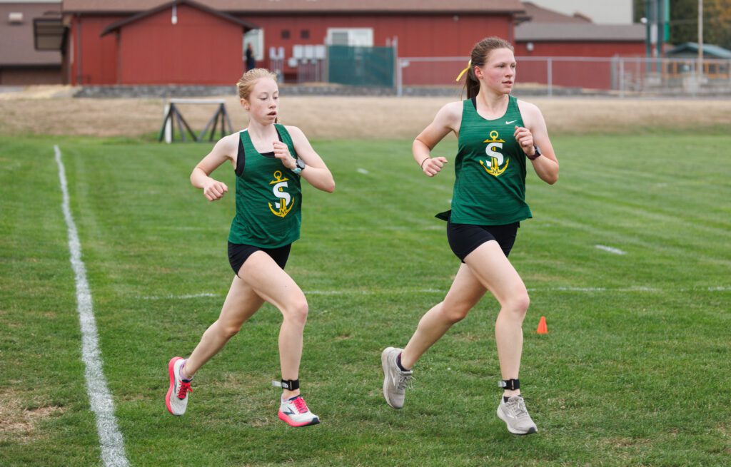 Sehome’s Sydney Harri, left, and Marcella Leita run side by side across the grass field.