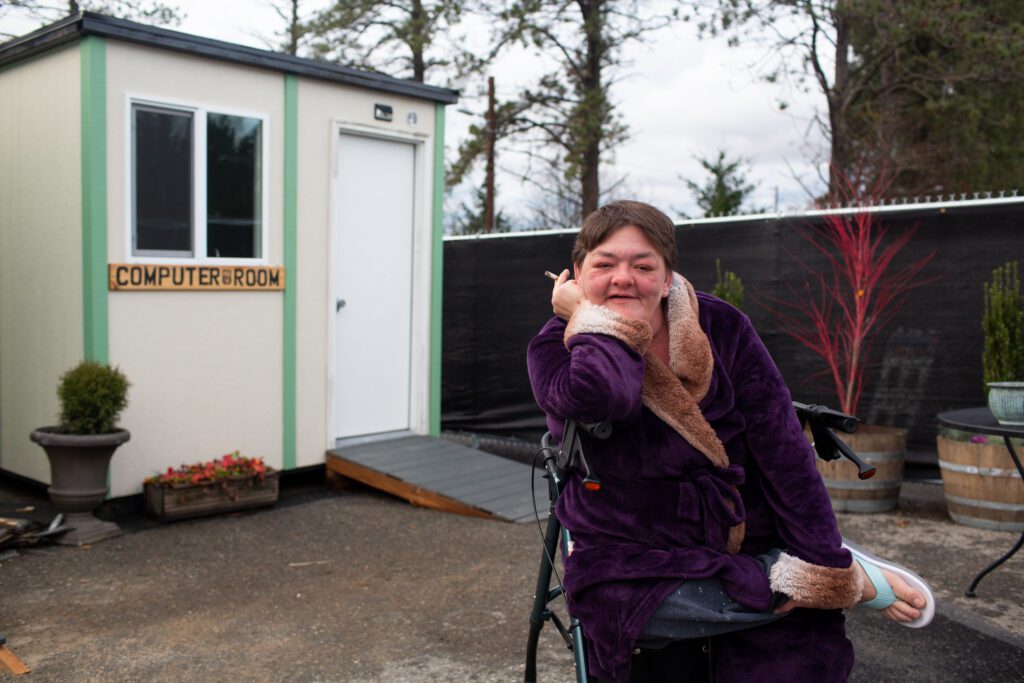 Peggy Lee Ramos sits outside of a small home with a cigarette.