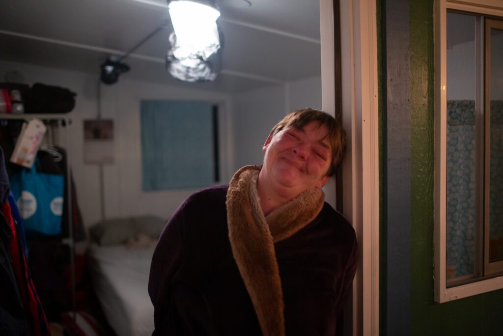 Peggy Lee Ramos stands in the doorway of her tiny home with a smile.