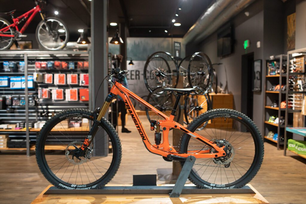 An orange mountain bike is on display at Transition Bike Co. near other shelves of cycling accessories.