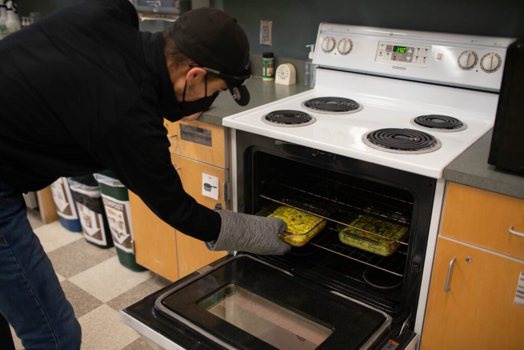 A Community Transition student puts a quiche in the oven next to another glass tray with a quiche.