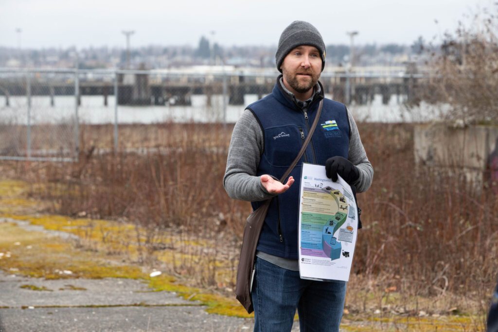 Ian Fawley, who does community outreach with the Washington Department of Ecology, holds up an infographic as he gestures with his free hand while talking.