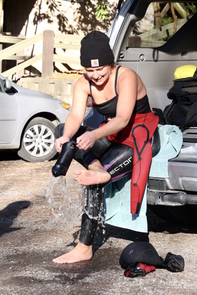 Water spills out as Kim Wiley removes her wetsuit booties as she sits on the back of her car.