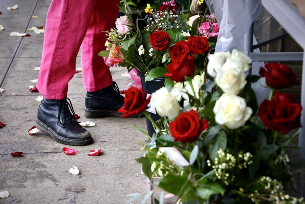 A customer wearing pink pants and black shoes are greeted with a trail of rose petals scattered along the sidewalk in front of the store.