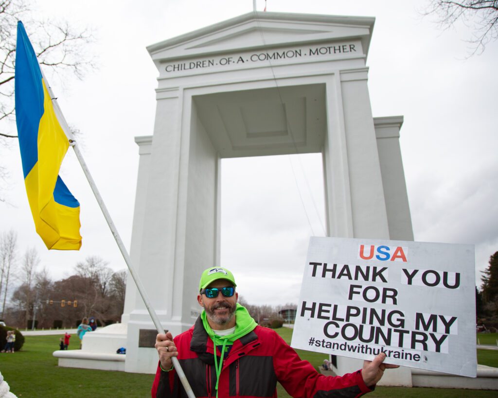 Ukrainian-American Vitaliy Baydak stands outside Peace Arch State Park with a Ukrainian flag and a sign thanking the U.S.A.