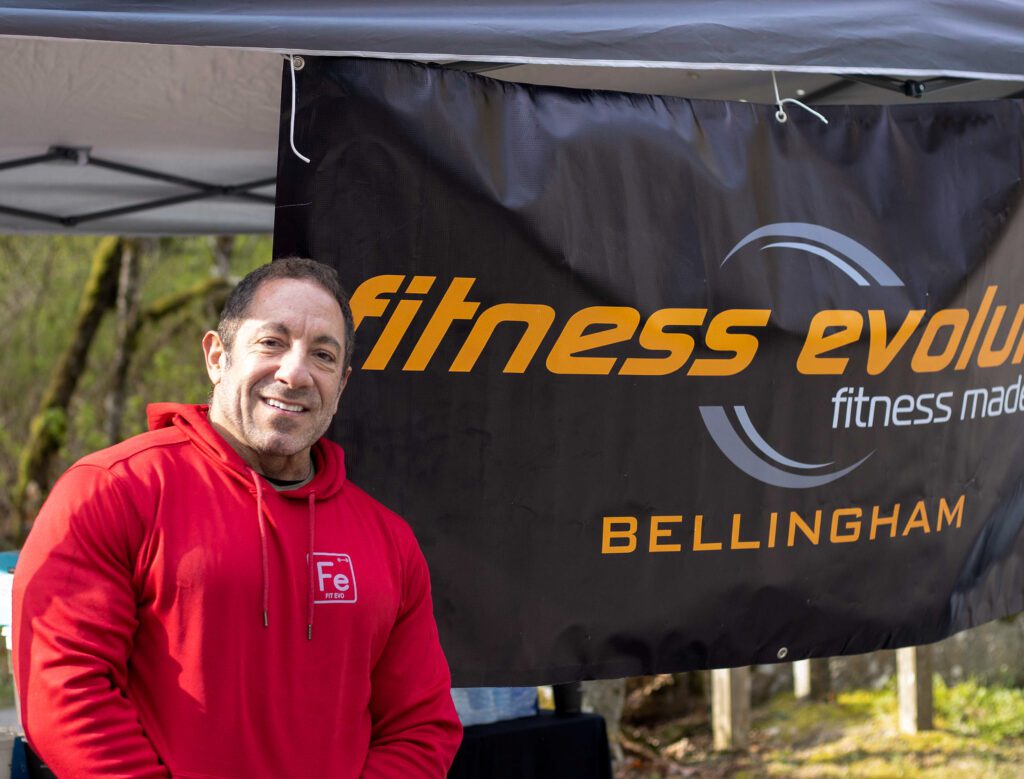 Steve Avila, the organizer of the trailhead patrol and owner of Fitness Evolution, stands next to the fitness evolution banner.