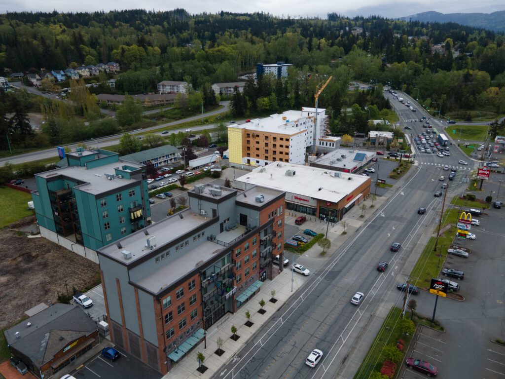 Several new, large apartment buildings have been constructed along Samish Way as many cars drive by the buildings.