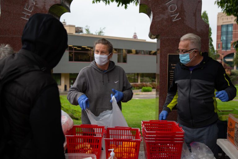 CAST volunteers Dionne Williams, left, and Karl Lien package a bag of sandwiches, fruit and other snacks from a row of red baskets.