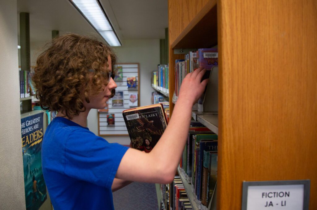 Aubri Blum pulls out fiction books from the shelves.