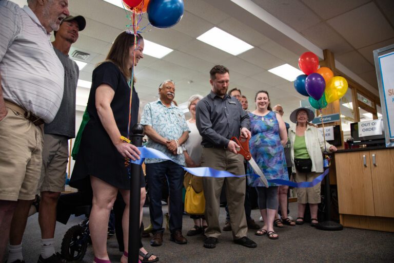 Branch manager Paul Fullner cuts the blue ribbon surrounded by balloons.