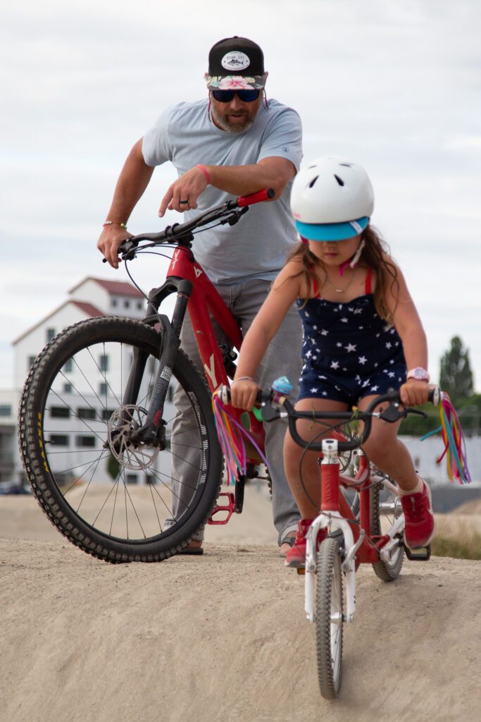 Reagan West encourages Sierra, 5, to ride her bike down the hill as he leans against his own bike.