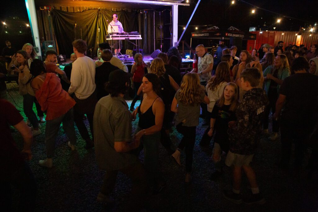 People dance to DJ Boombox Kid's set as lights shine on him.