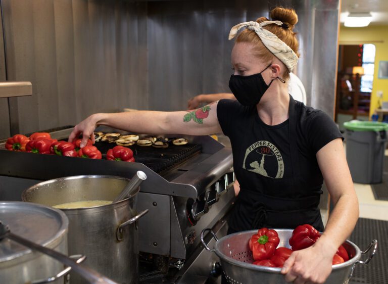 Pepper Sisters co-owner Kelsey Andrews adds red peppers to the grill while holding a bowl of red peppers.