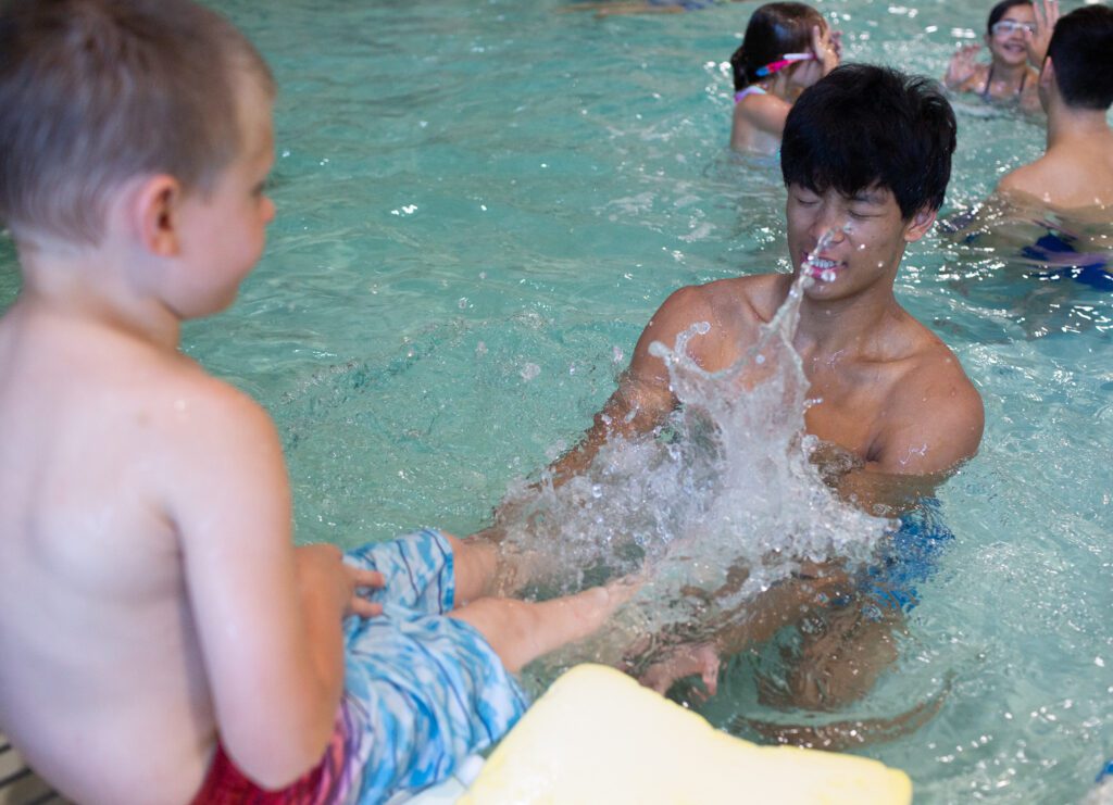 Nathan Chen closes his eyes as he is splashed by student Michael, 4, while practicing straight-legged kicking from the wall.