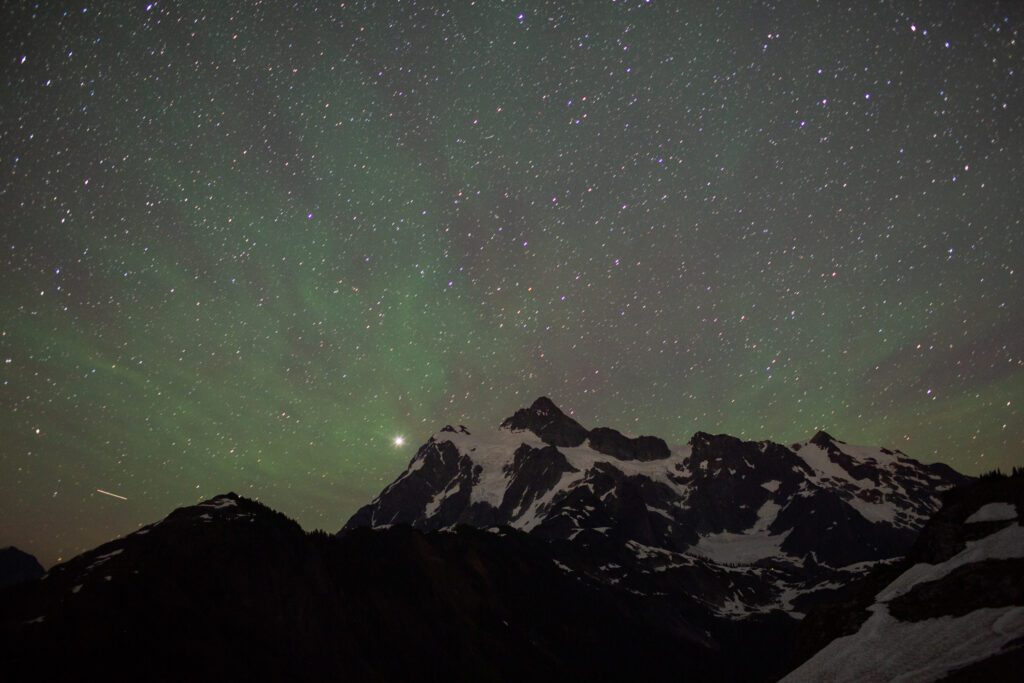 Stars shine over Mount Shuksan as green lights shine on thee sky.