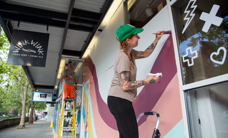 Private Eye tattoo studio owner Jes Bonin, right, and Will Marks cover the boarded windows of WinkWink Boutique with a colorful mural.