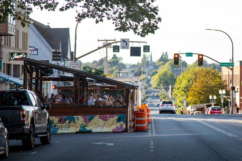 People dine in the parklets of restaurants as cars drive by.