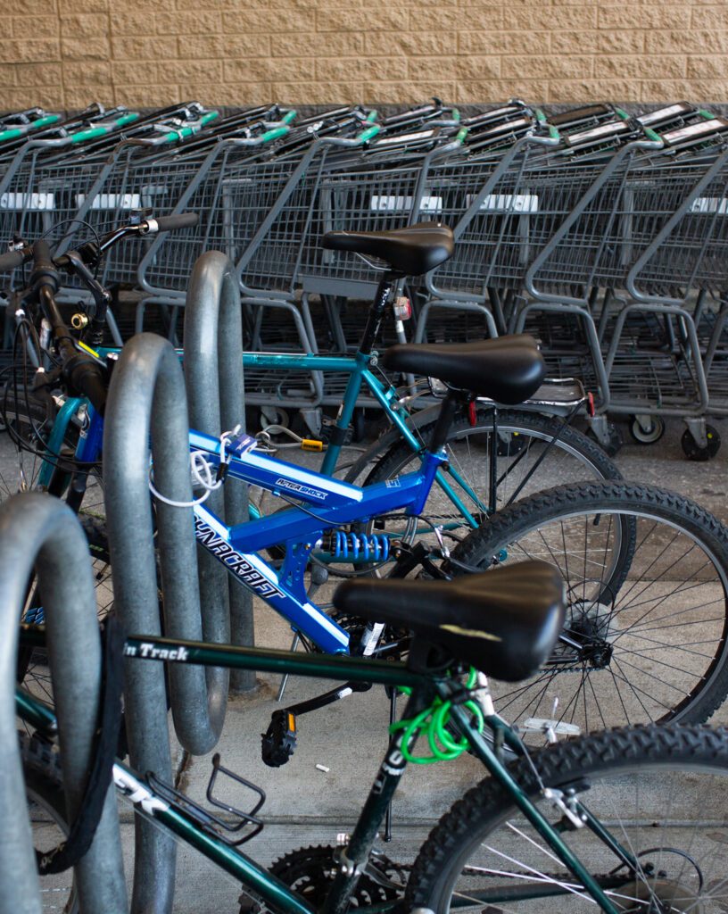 Bikes parked up on a small rack outside of a grocery store next to shopping carts.