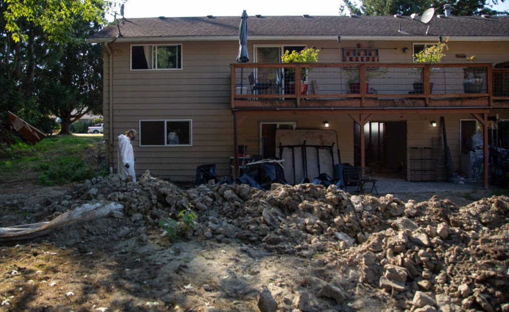 Levi Brown walks around the back of the house, with asbestos laid out on the ground.