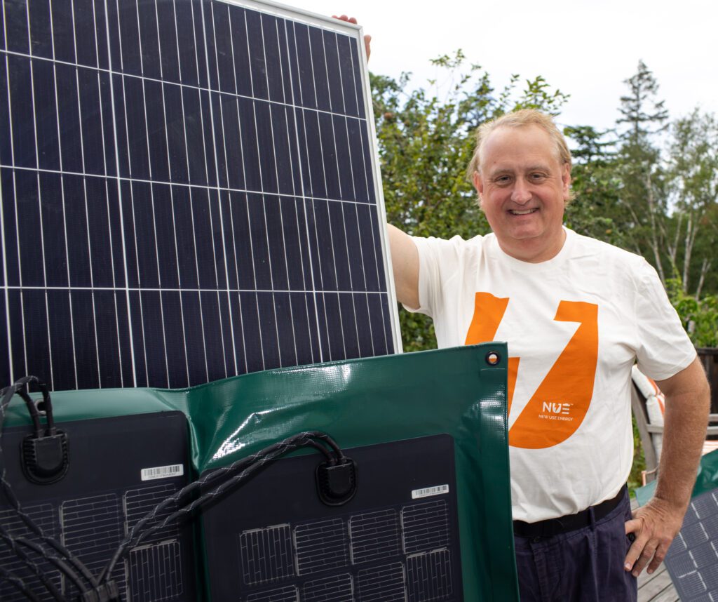 Paul Shmotolokha stands with solar panels with a smile.