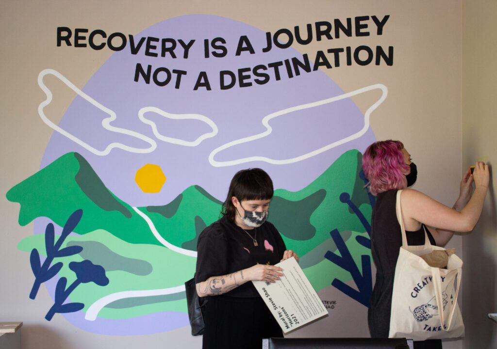 Jessyca Murphy, left, and Emily Campbell hang a plaque crediting Stevie Shao next to a stylistic mural.