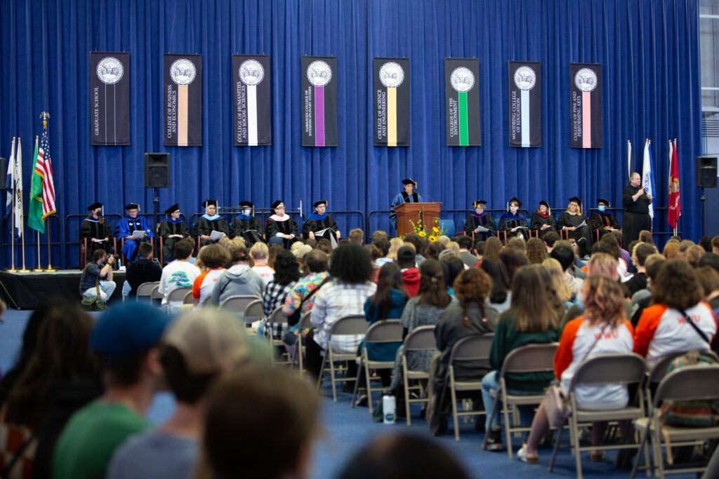 Faculty Senate President Lysa Rivera speaks to new students at the 2022 Convocation as her faculty members sit side by side behind her.