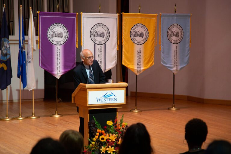 President Sabah Randhawa speaks to students, faculty and staff of Western Washington University from behind a wooden podium.