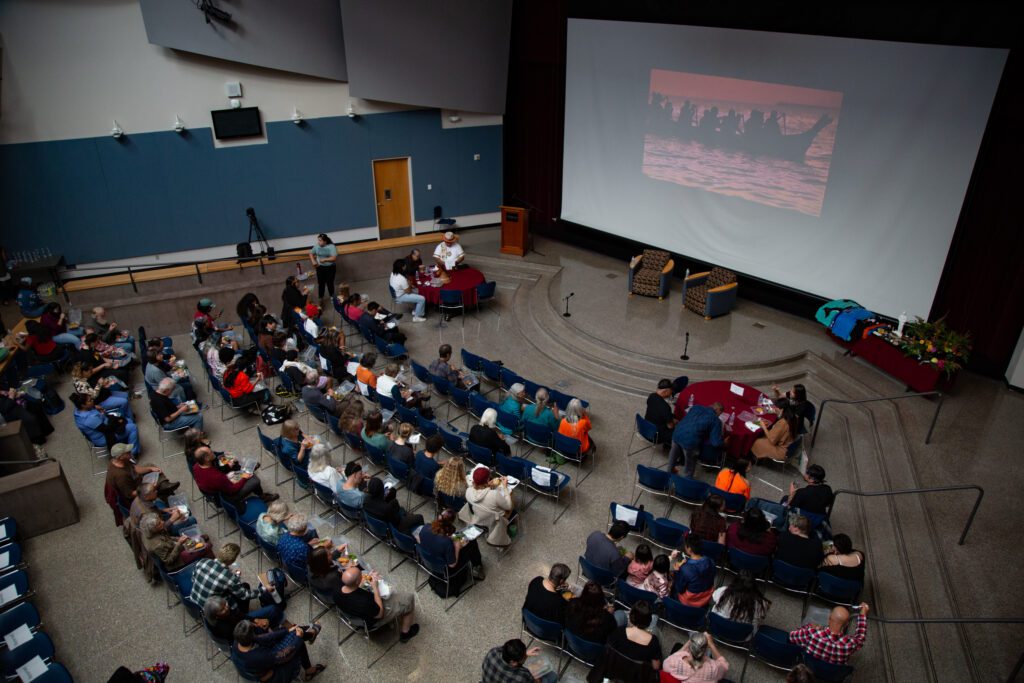 Dozens eat a traditional salmon dinner while watching films created by the Children of the Setting Sun Productions on a large projector.