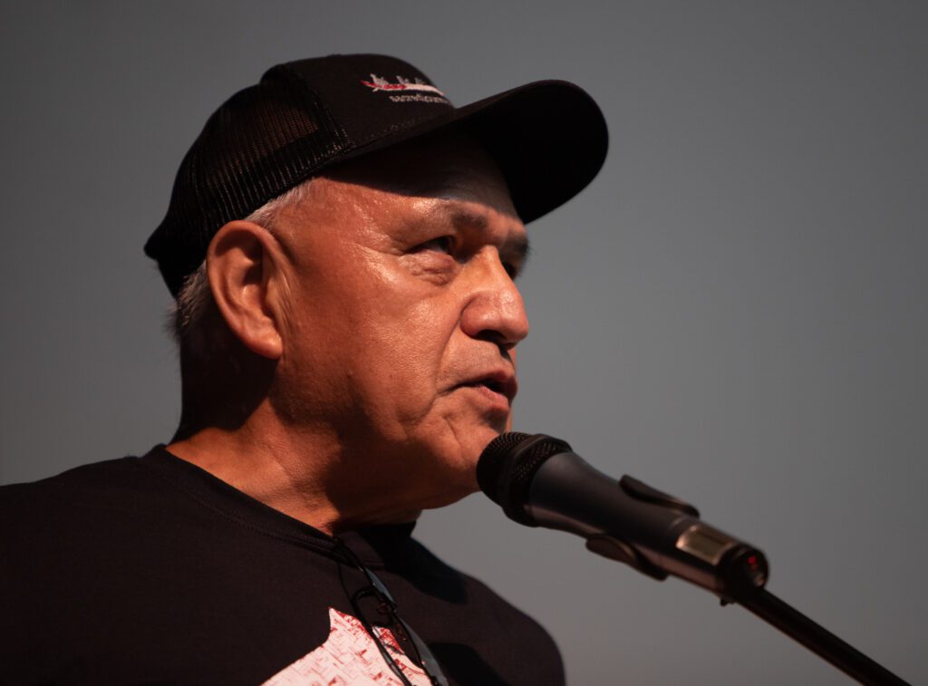 Darrell Hillaire, a member of the Lummi Nation and the executive director of Children of the Setting Sun Productions, speaks to a packed crowd with a microphone.