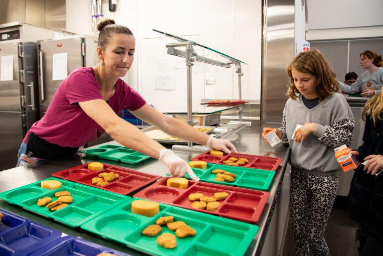 Food service assistant Jessica Johnson hands out colorful trays of chicken nuggets and garlic bread for students at Alderwood Elementary School.