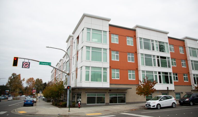 The roadside of Eleanor Apartments with multiple cars parked next to the bright orange and white building.