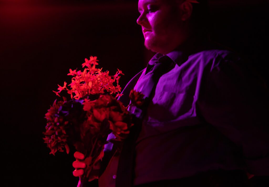 Rax Organa, a guest performer and friend of Victoria Sprong Chue, carries a bouquet of flowers on stage during his performance.