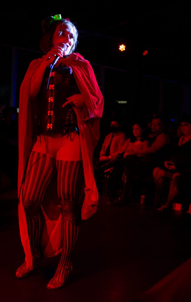 Veronica sings and dances with her back turned to the audience while donning a red cape.