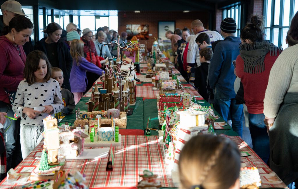 Families and friends look at a table showcasing gingerbread houses.